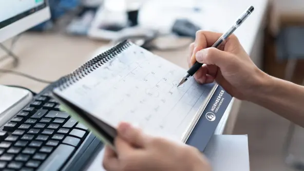 Hand mit Stift umkreist Datum in einem Kalender der NÜRNBERGER Versicherung