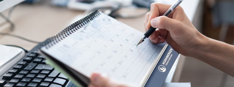 Hand mit Stift umkreist Datum in einem Kalender der NÜRNBERGER Versicherung