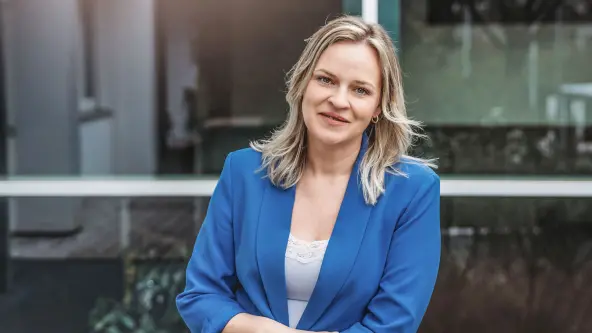 Junge Frau mit blonden Haaren und blauem Blazer blickt lächelnd in die Kamera