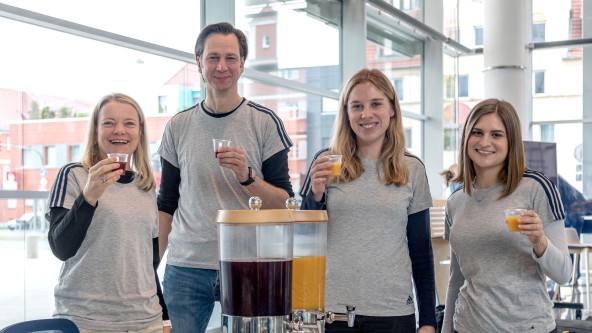 4 Personen in grauem Shirt trinken ein orangefarbenes Getränk