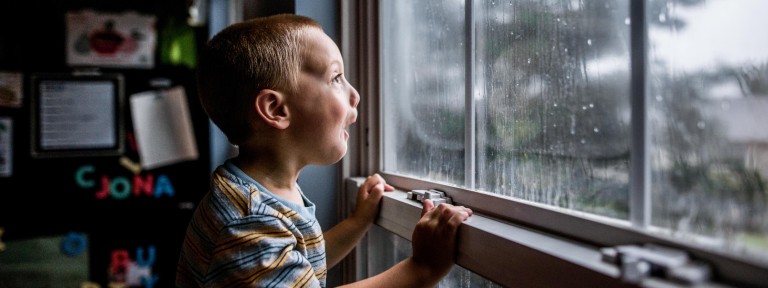 Kleiner Junge sitzt staunend vor einem Fenster und blickt nach draußen