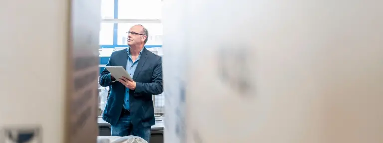 Mann mittleren Alters im Anzug und mit Brille hält Tablet in der Hand