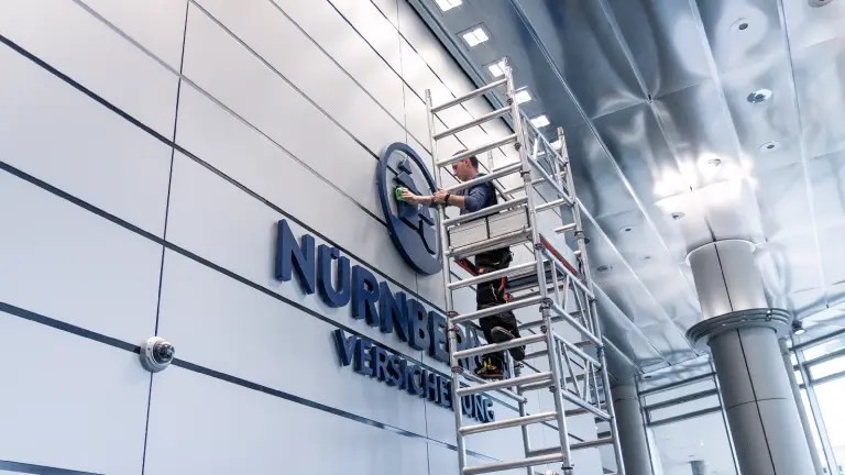 Mann hängt auf einem Gerüst stehend das Logo der NÜRNBERGER Versicherung in Gebäude auf
