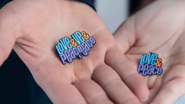 Zwei Hände halten jeweils einen Pin auf dem Love & Peace steht