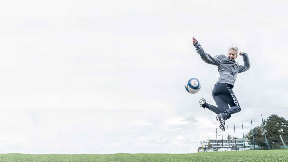 Junge Frau springt hoch und kickt dabei nach einem Fußball
