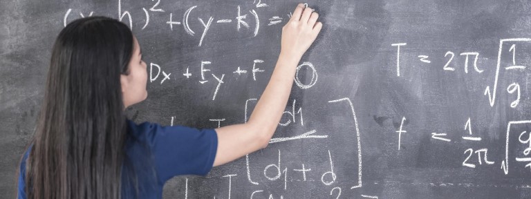 Mädchen steht an einer Tafel und rechnet eine Mathematik-Aufgabe