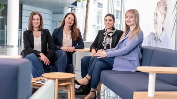 4 junge Frauen sitzen in einem offenen Büroraum zusammen
