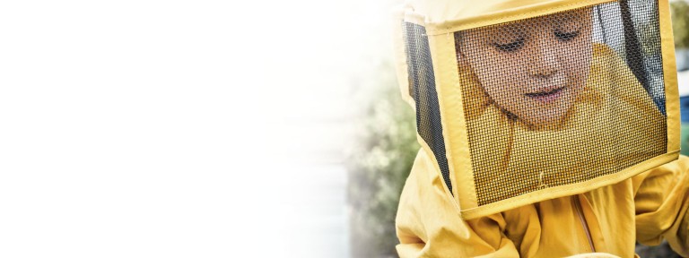 Ein Junge trägt Imkerschutzanzug und hat eine Biene auf der Hand sitzen