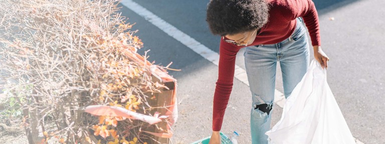 Junge Frau mit schwarzen Haaren sammelt Müll am Straßenrand auf