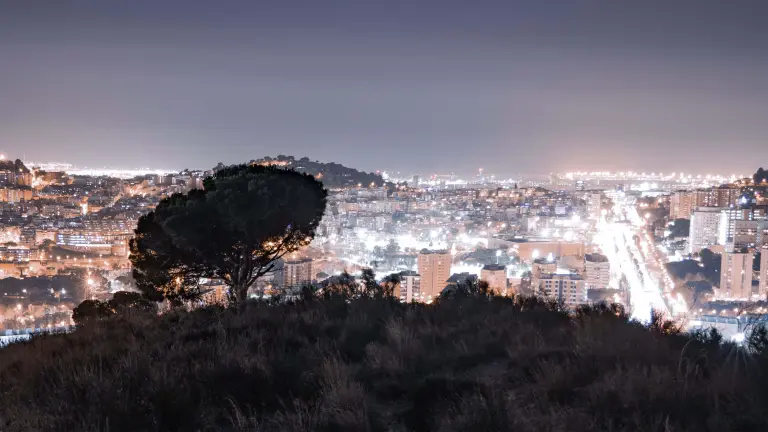 Blick von einem Berg auf eine hell aufleuchtende Stadt bei Nacht